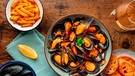 Ein Teller mit Miesmuscheln, ein Schälchen Pommes, Zitrone, Baguettescheiben und ein Glas Weißwein stehen auf einem Holztisch | Bild: mauritius images / Ilya Solovyev / Alamy / Alamy Stock Photos